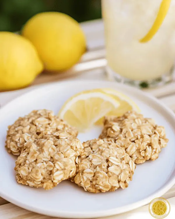 Three lemon oatmeal no bake cookies served on white plate with glass of lemonade and fresh lemon garnish